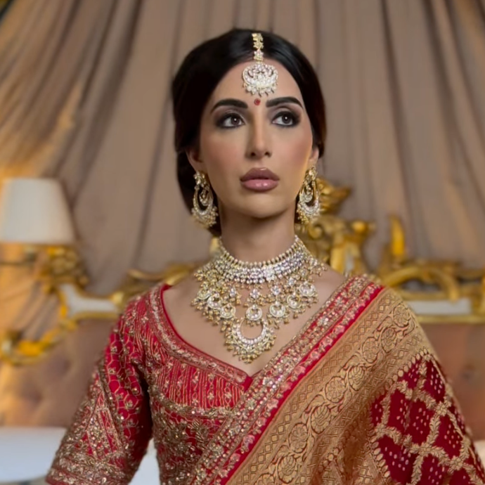 Woman in traditional red and gold embroidered outfit with jewelry against a decorative background